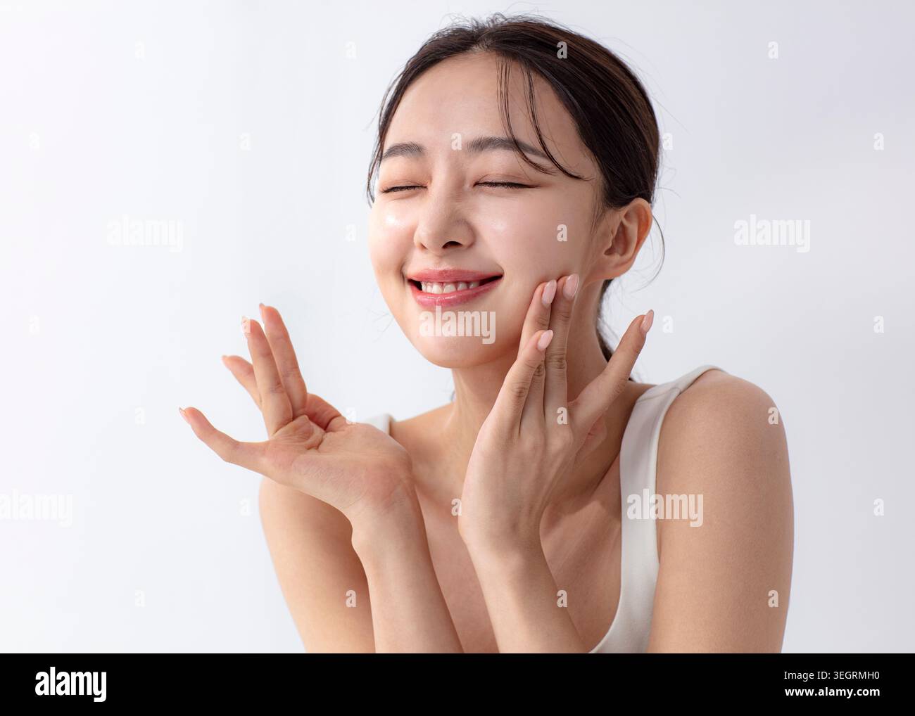 Eine junge Frau mit geschlossenen Augen, die ihr Gesicht sanft mit den Händen berührt, in einer entspannten und ruhigen Umgebung. Stockfoto