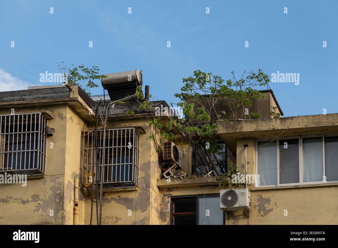 HAINING, CHINA - 9. MAI 2026: Ein verwittertes gelbes Wohngebäude in einer städtischen Umgebung mit abblätternder Farbe, Metallgittern und invasiven Elementen Stockfoto