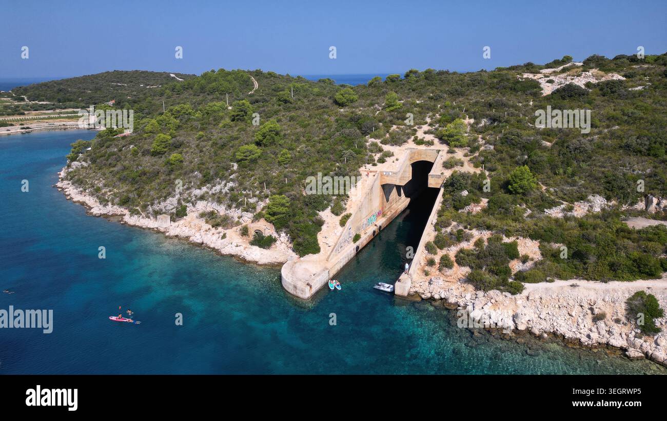 Aus der Vogelperspektive auf die jugoslawische Armee unterirdische Bootsunterkunft Potkop Parja, die in die felsige Küste mit türkisfarbenem Wasser und üppigen grünen Hügeln Rogac gehauen wurde Stockfoto