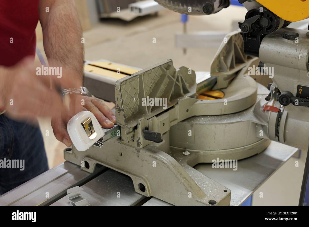 Facharbeiter, der ein Metallprofil mit einem einziehbaren Bandmaß und einer Gehrungssäge in einer Werkstatt misst und mit Präzision an einem Bauprojekt arbeitet Stockfoto