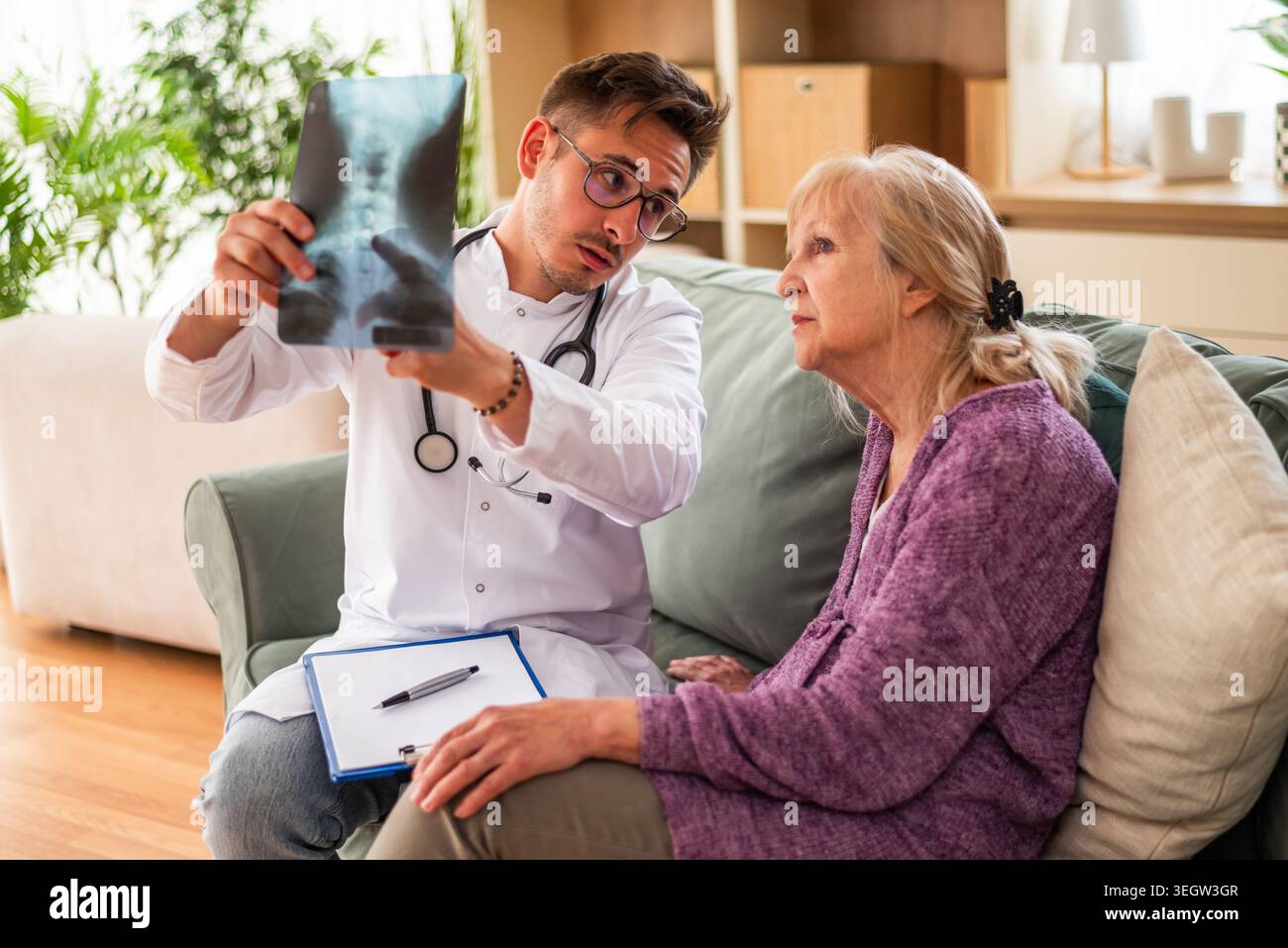 Der Hausarzt untersucht ein Röntgenbild mit einer älteren Frau zu Hause. Professionelle Gesundheitsförderung für ältere Menschen. Stockfoto