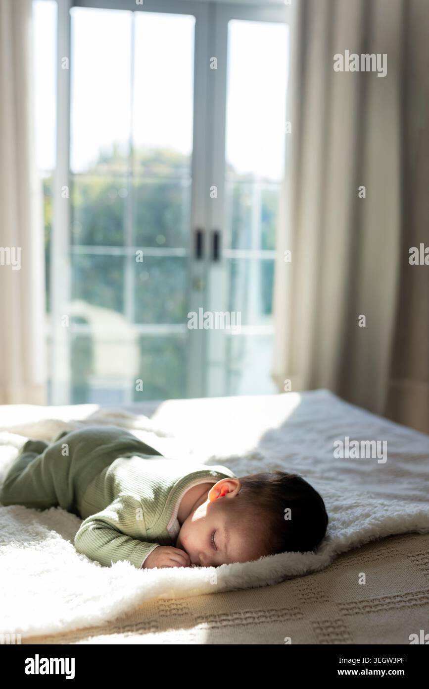 Säuglingsmädchen schlafend im hellgrünen Einteiler auf Plüschdecke durch Glasschiebetüren Stockfoto