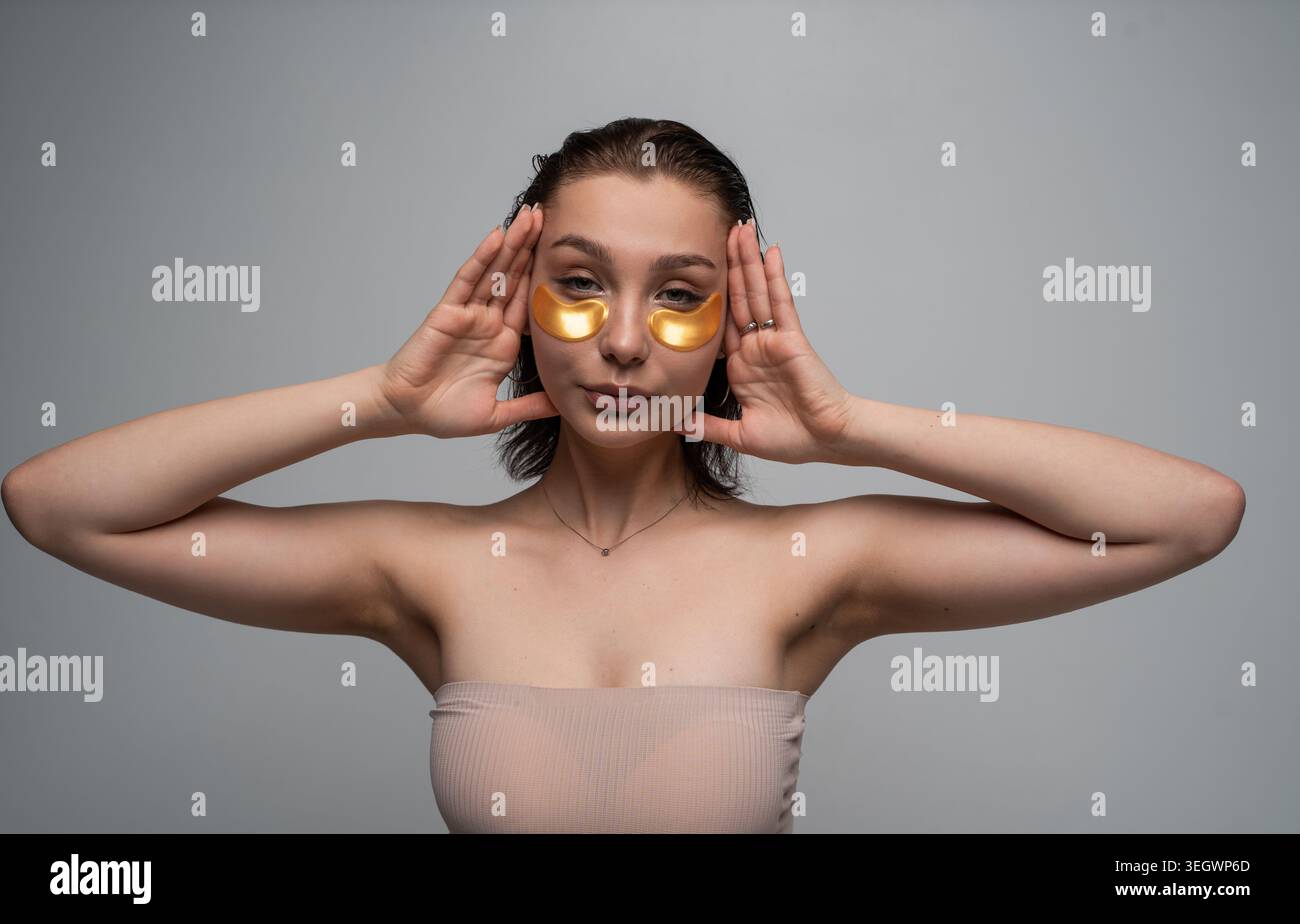Frau, die goldene Flecken unter den Augen aufträgt, um Kollagen und Feuchtigkeit zu spenden, pflegt ihre Haut und den empfindlichen Bereich um die Augen für Schönheit und Stockfoto