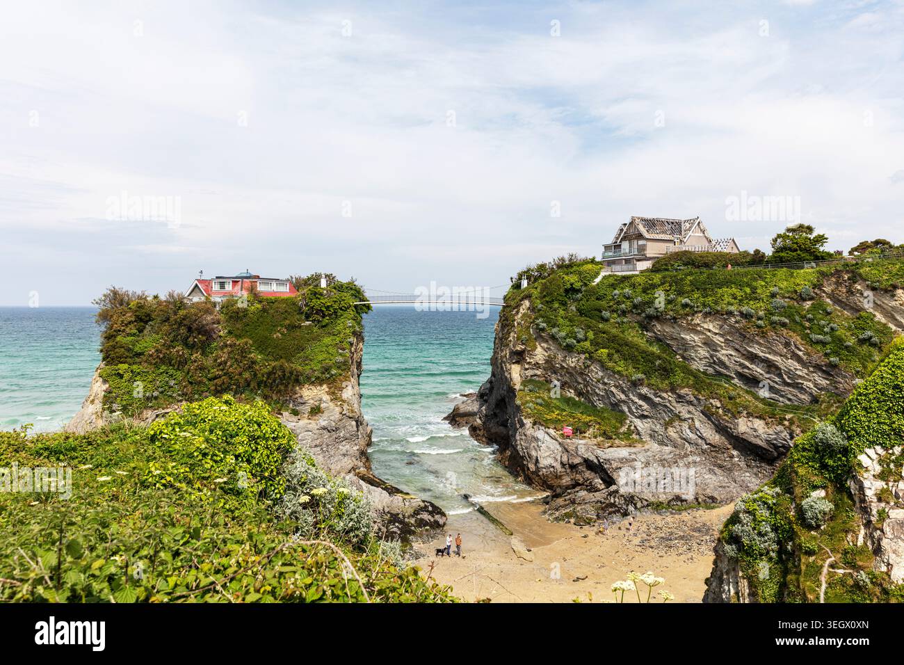 Dramatische Küstenszene in Newquay, Cornwall, mit zwei Häusern auf separaten felsigen Klippen, die durch eine enge Bucht geteilt sind. Unten ein Sandstrand mit Stockfoto