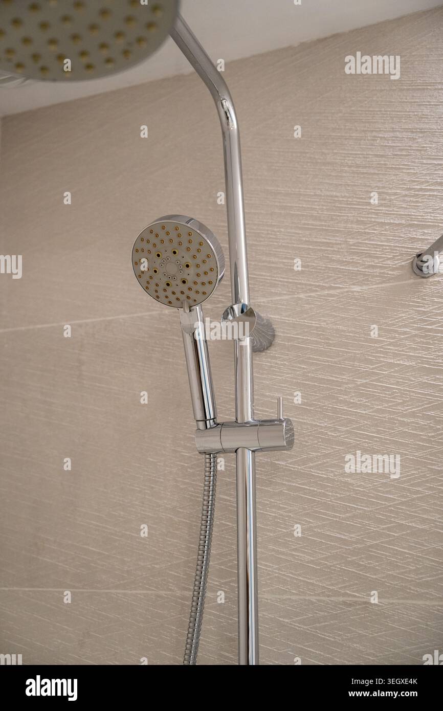Moderne Chrom-Duschvorrichtung mit Regenfall über Kopf und Handspray, montiert an strukturierten beigefarbenen Wänden, elegante, moderne Badezimmerdetails Stockfoto