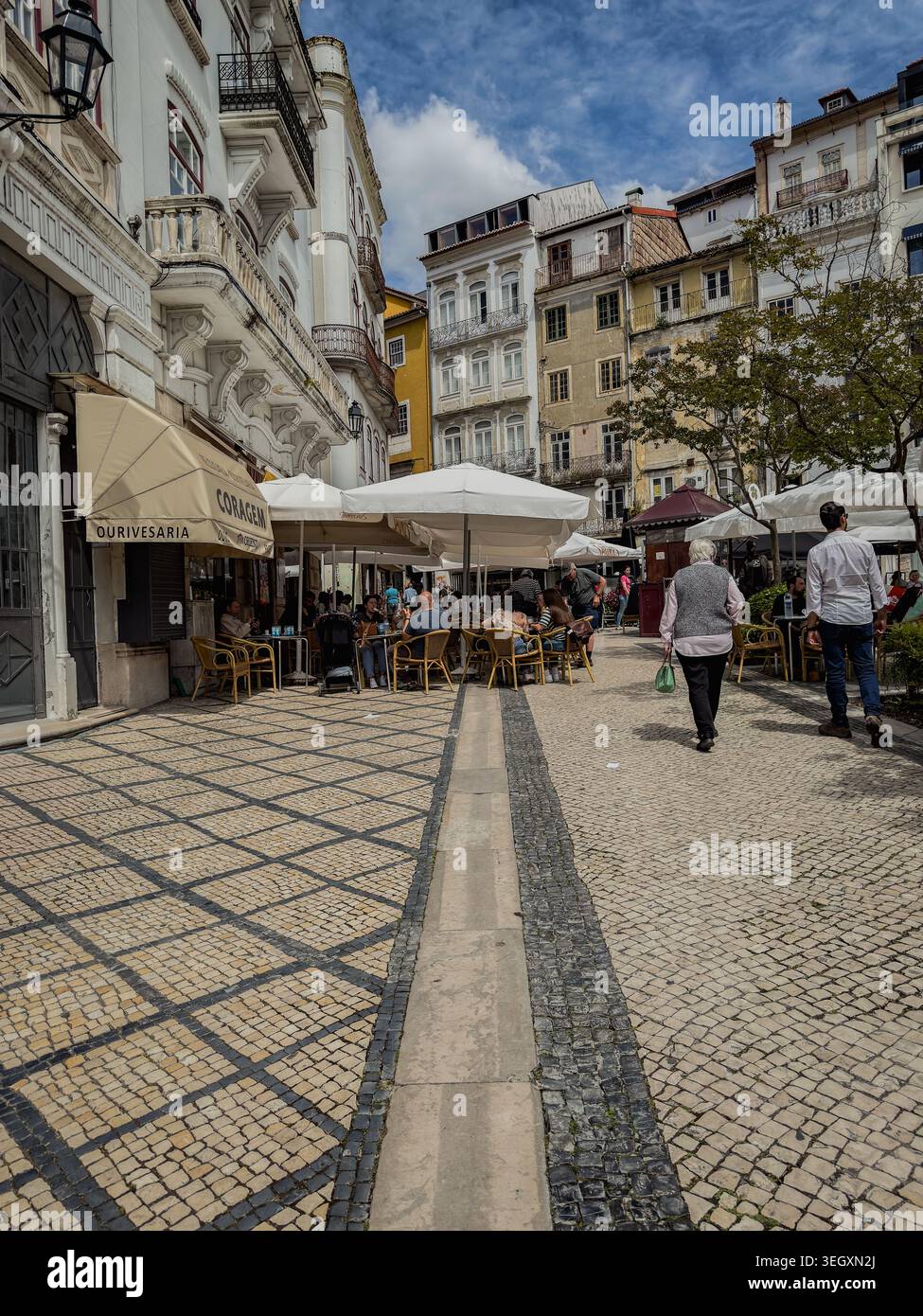 Belebte Café-Szene im historischen Zentrum von Coimbra, Portugal, mit Fußgängern, gemusterten Kopfsteinpflasterstraßen und charmantem europäischem Archit Stockfoto