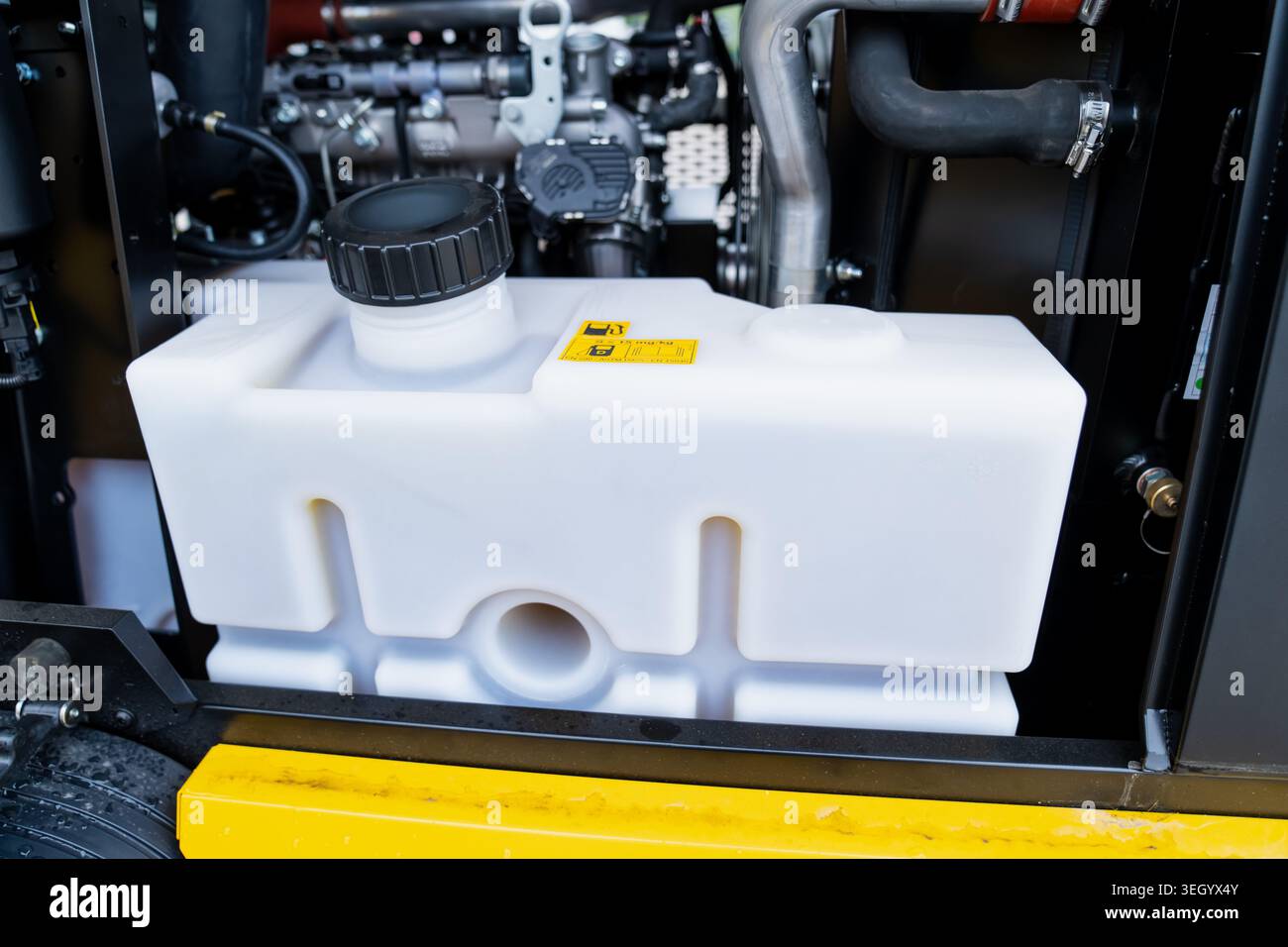 Halbtransparenter, weißer Kunststoff-Kühlmittelausgleichsbehälter mit schwarzem Schraubverschluss, der in einem Dieselmotorraum für schwere Maschinen montiert ist Stockfoto