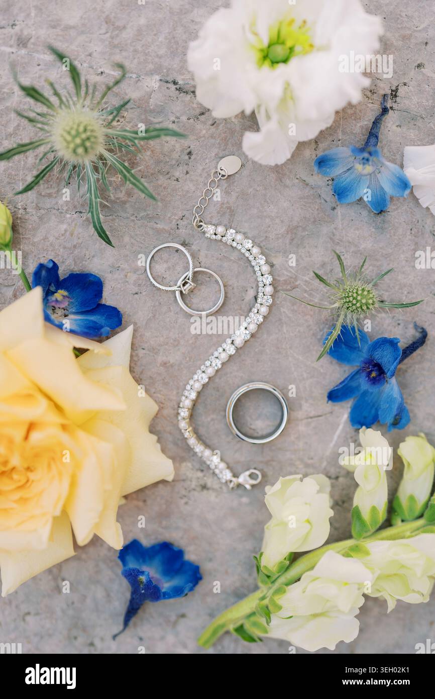 Hochzeitsschmuck und Ringe mit bunten Blumen auf Steinoberfläche Stockfoto