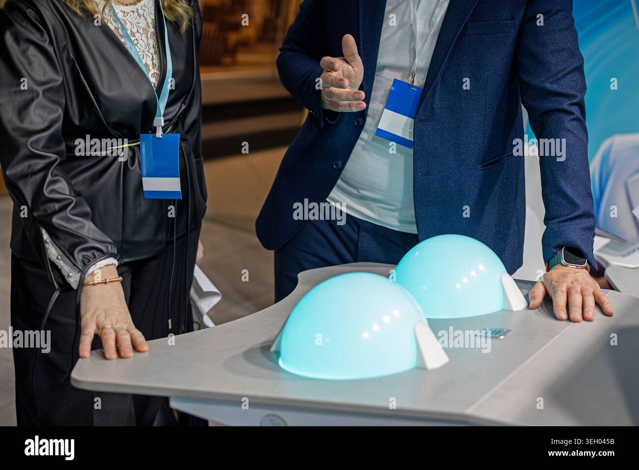 Fachleute diskutieren auf der Expo über Medizinprodukte. Geschäftsleute mit Konferenzabzeichen diskutieren über ein futuristisches Gesundheitsgerät mit Glowing Stockfoto