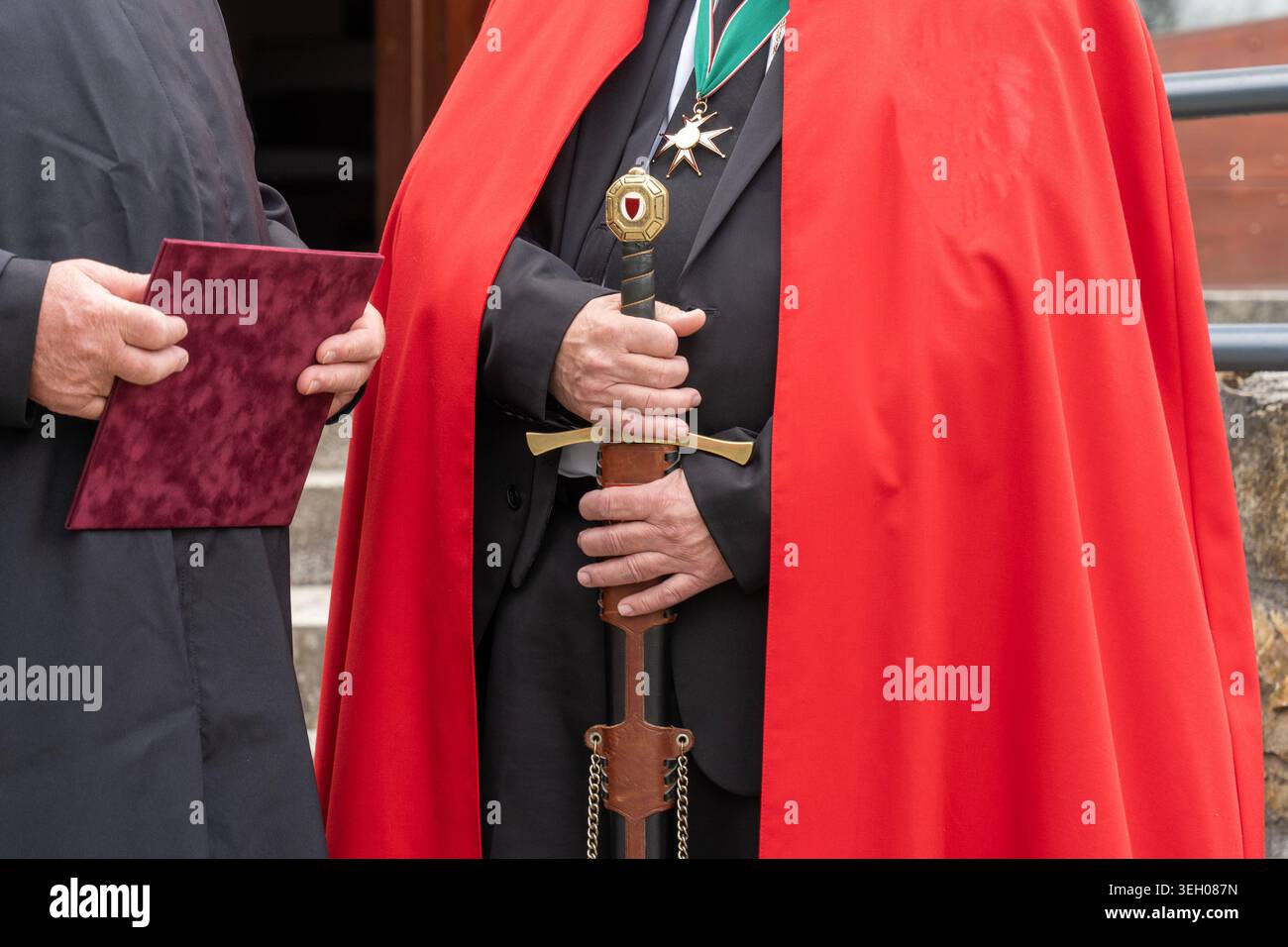 Eine Figur in zeremonieller Kleidung eines modernen Rittertums, die ein mittelalterliches Schwert in einem roten Mantel hält Stockfoto