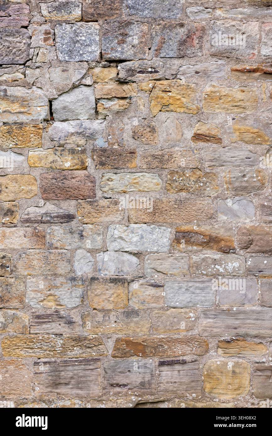 Verwitterte Steinmauerstruktur mit gemischten Sandsteinblöcken und Mörtel aus einem alten Gebäude außen, geeignet für Architektur und Hintergrund Stockfoto