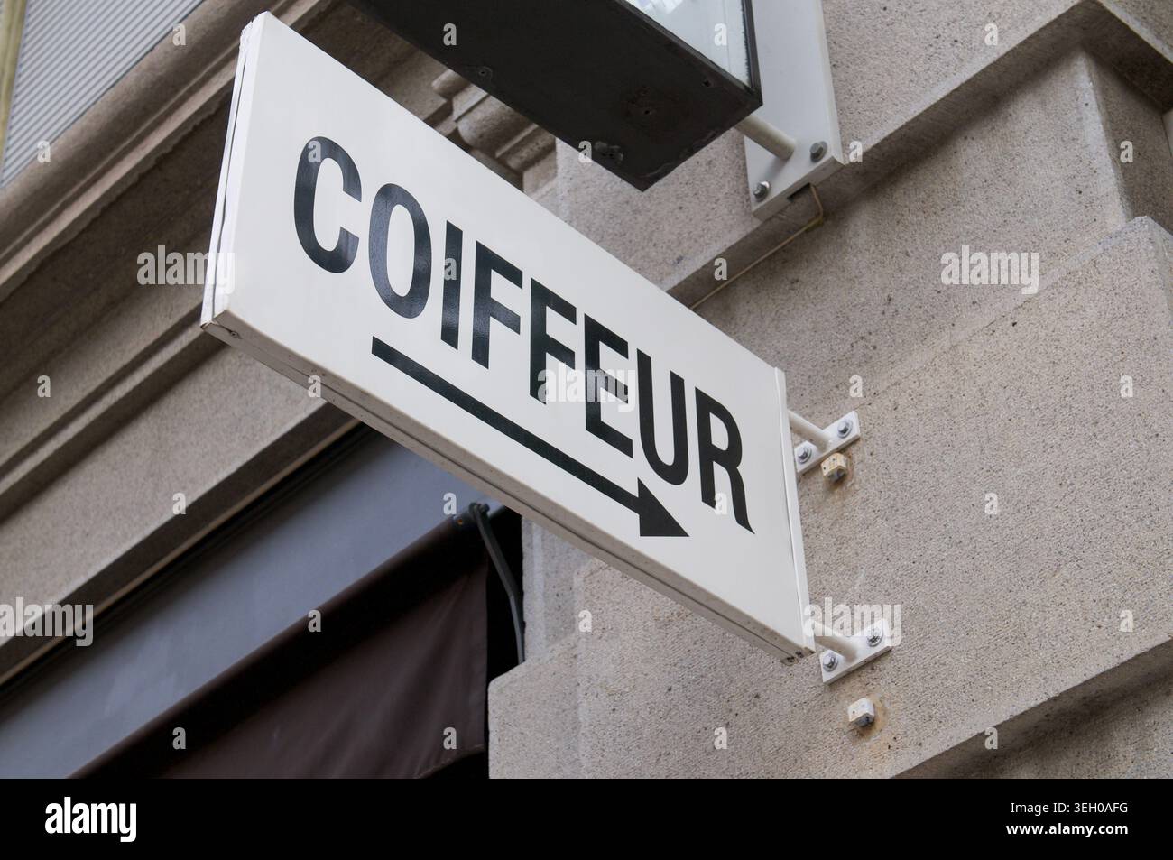 Weißes minimalistisches Außenschild mit schwarzem Text Coiffeur und Pfeil, montiert auf einer klassischen Betonwand. Friseur, französischer Friseursalon Stockfoto