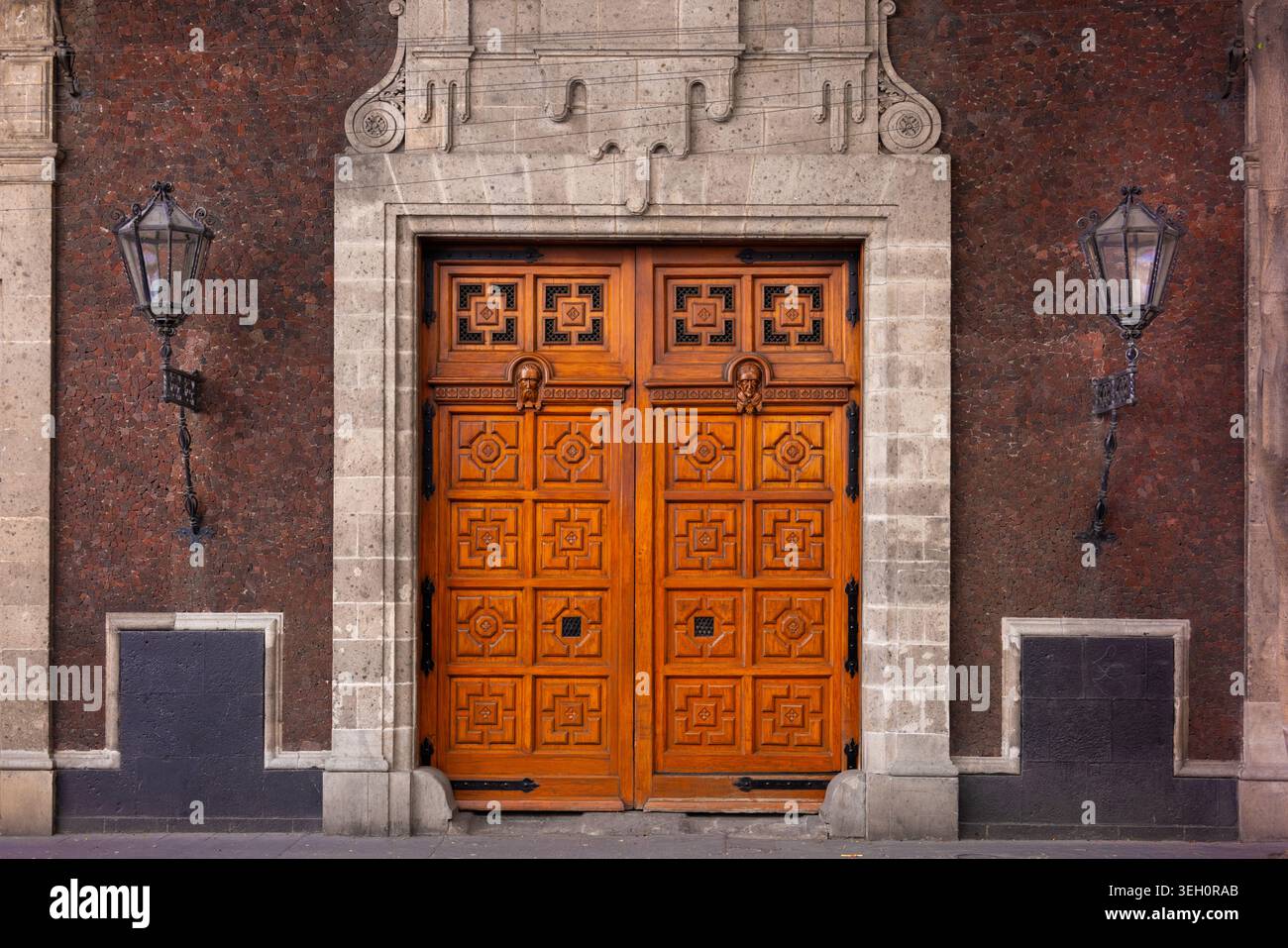 Blick auf kunstvoll geschnitzte Holztüren, flankiert von Vintage-Laternen an einer historischen Steinfassade in Mexiko-Stadt, Mexiko-Stadt, Mexiko. Stockfoto