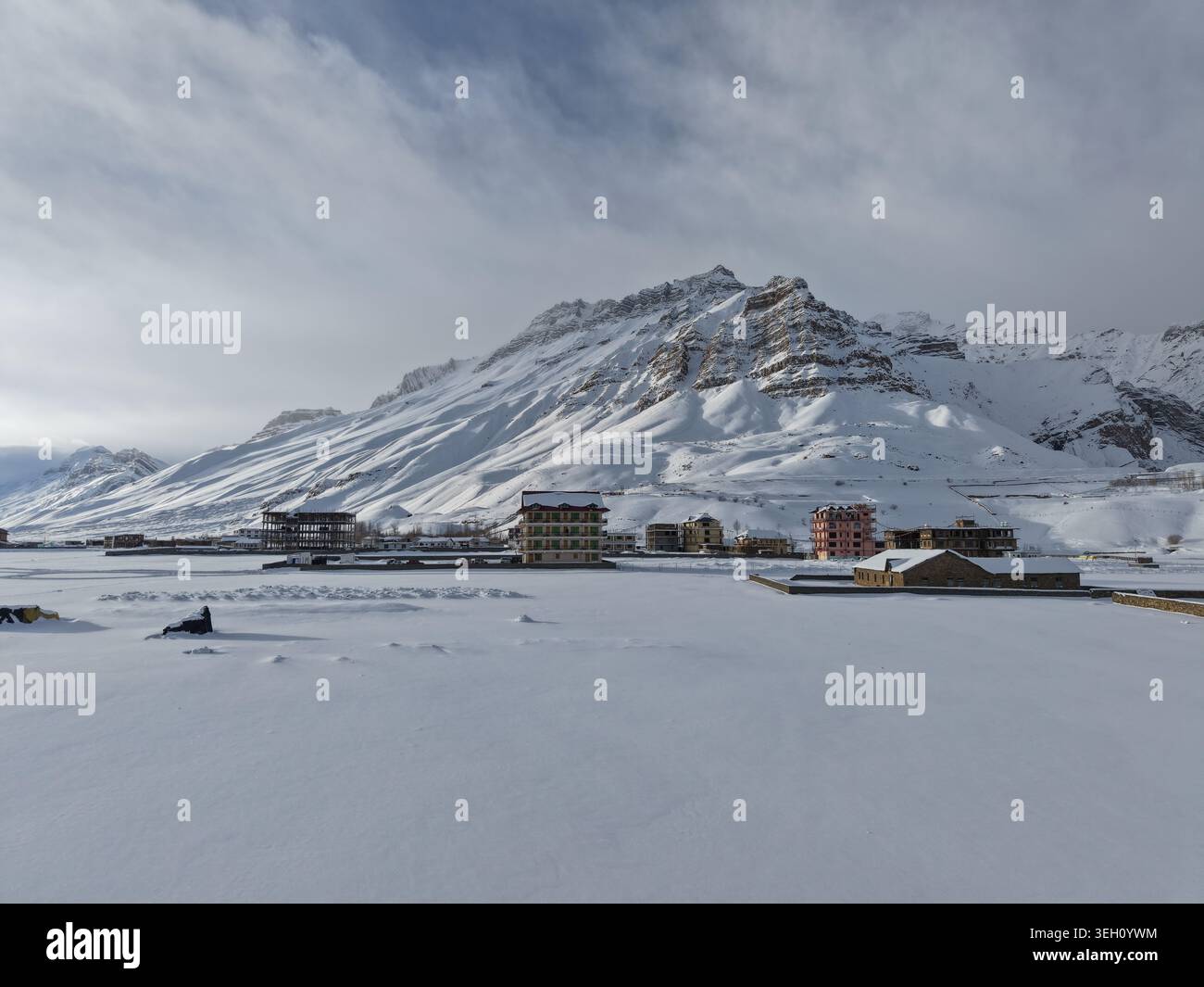 KAZA, Indien - 28. Januar 2026: Blick auf das Spiti-Tal mit schneebedeckten Gebäuden und majestätischen Gipfeln des Himalaya unter bewölktem Winterhimmel. Stockfoto