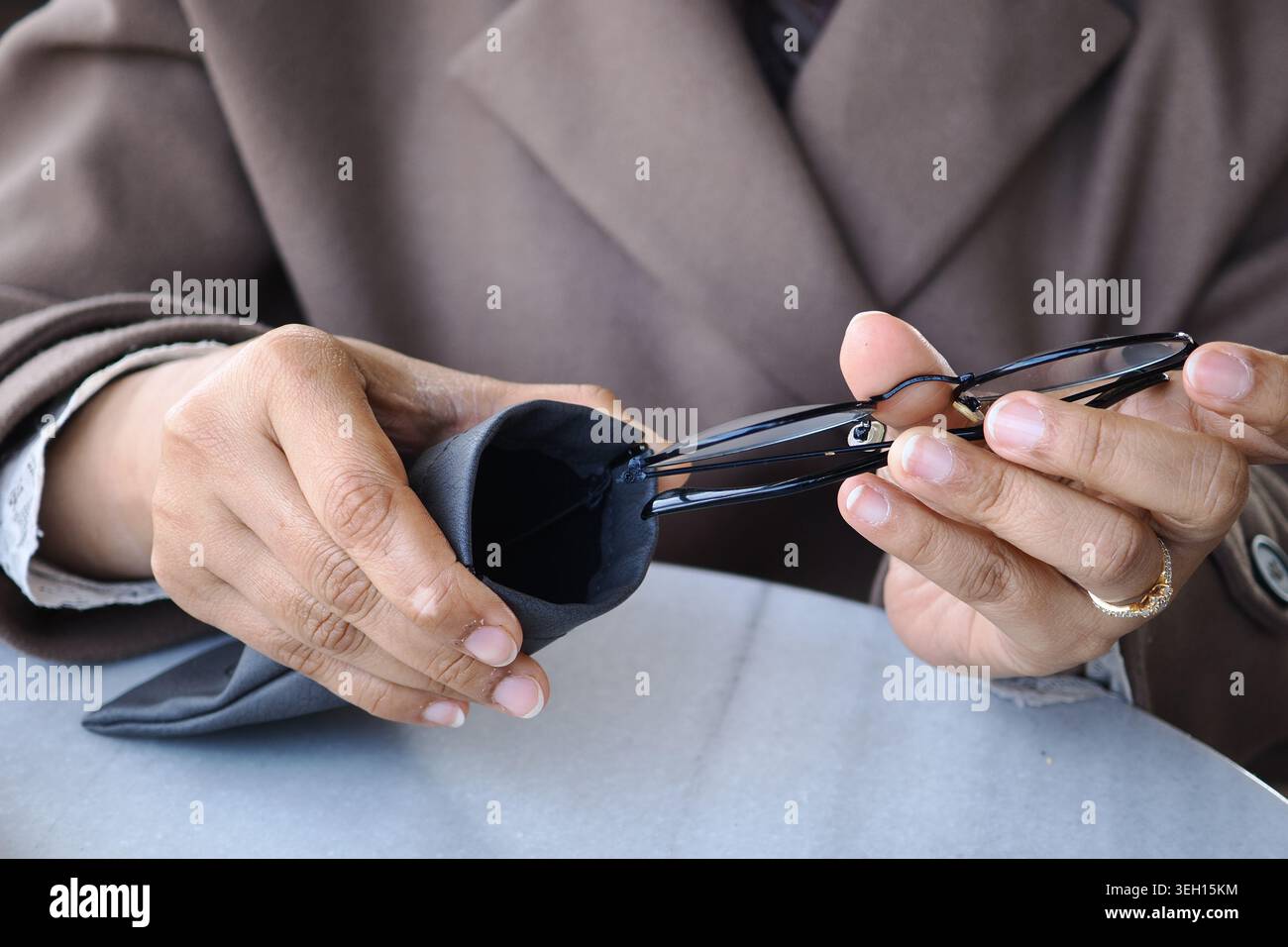 Hände, die eine Brille halten und eine Koffer an einem Tisch Stockfoto