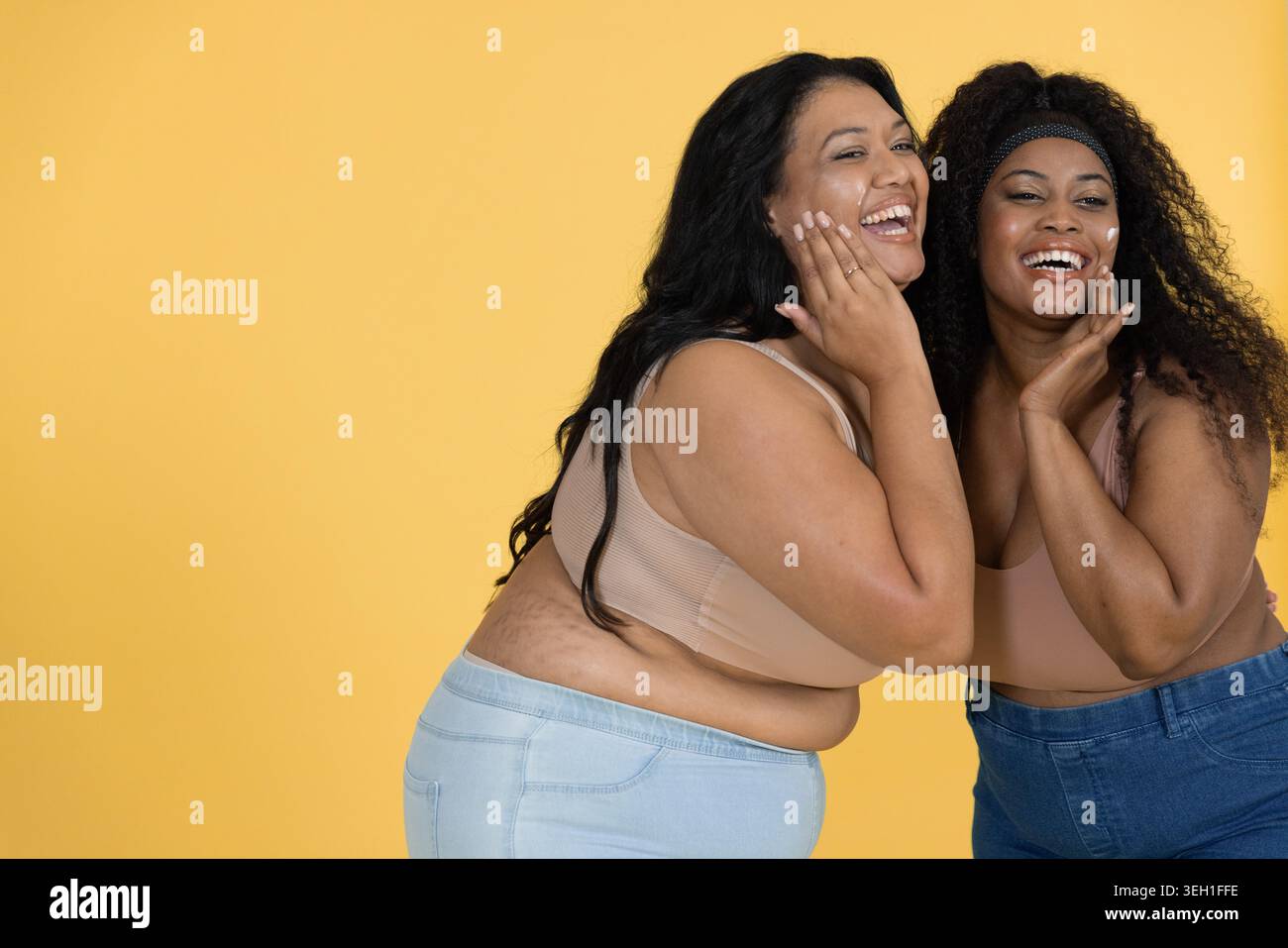 Zwei weibliche Freunde aus der Mitte des Erwachsenen posierten und lachten im Studio mit hautfarbenen Oberteilen, blauem Jeans-Stirnband Stockfoto
