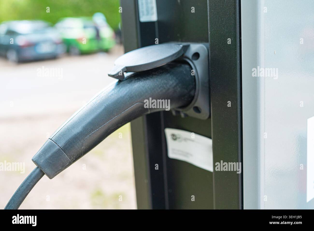 Anschluss für das Ladegerät für Elektrofahrzeuge mit verschwommenem Parkplatzhintergrund. Grüne Technologie, saubere erneuerbare Energien, Lebensstil der Zukunft, Makroansicht. Stockfoto