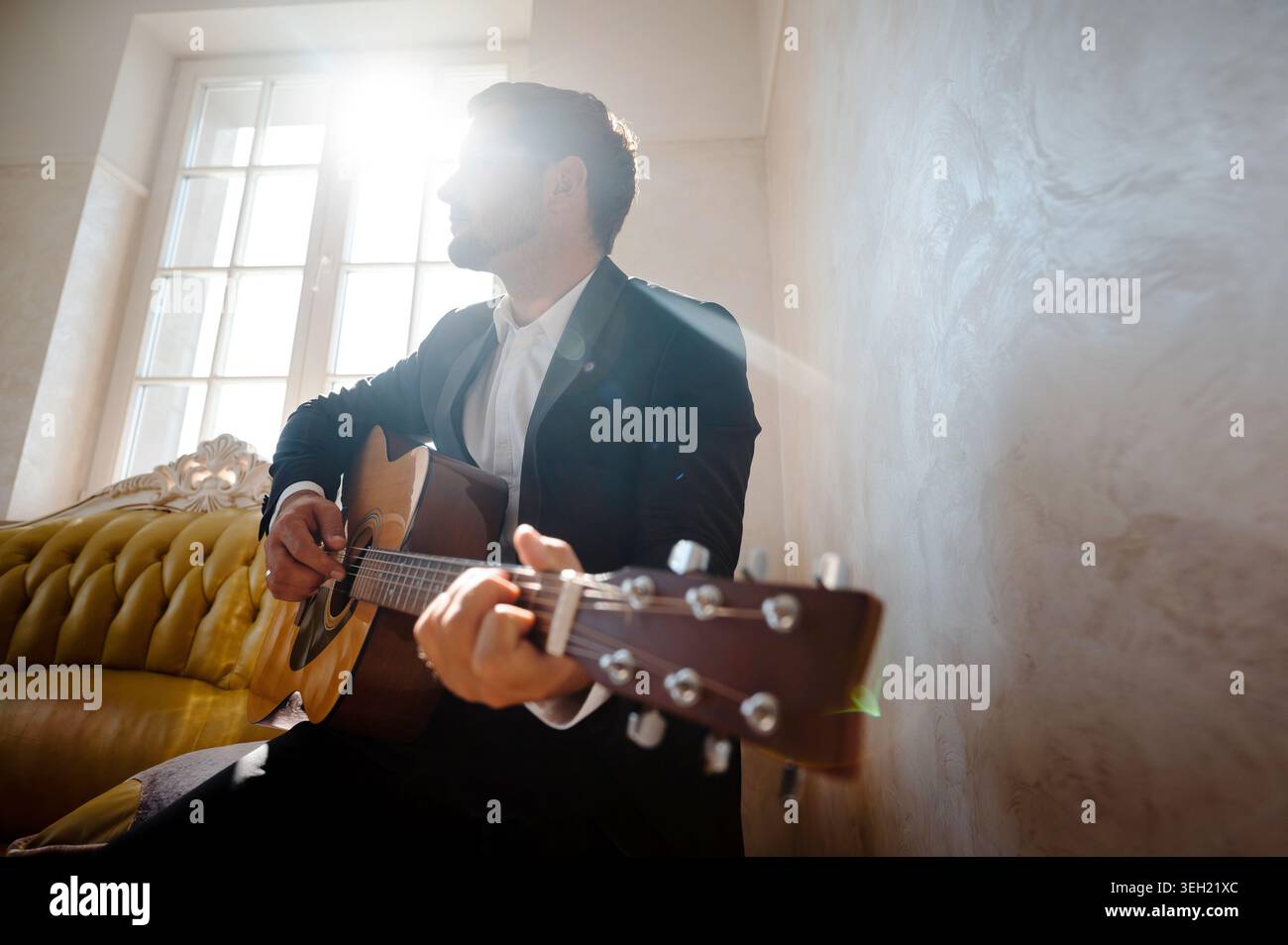 Hübscher junger Mann, der im Wohnzimmer Gitarre spielt Stockfoto