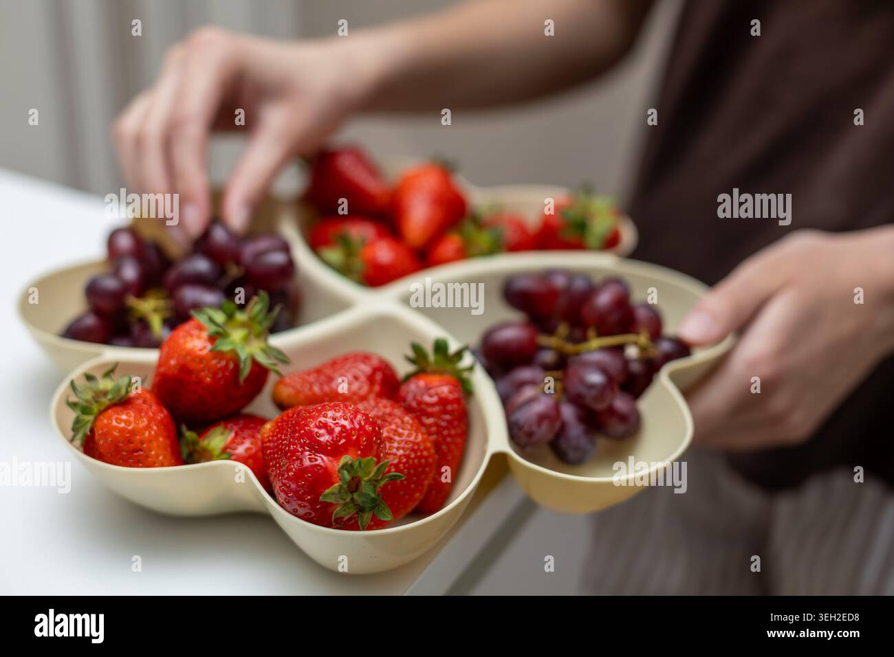 Frische Erdbeeren und Trauben in Serviertablett. Nahaufnahme der Hände, die ein geteiltes Tablett mit frischen Erdbeeren und roten Trauben für gesund halten Stockfoto