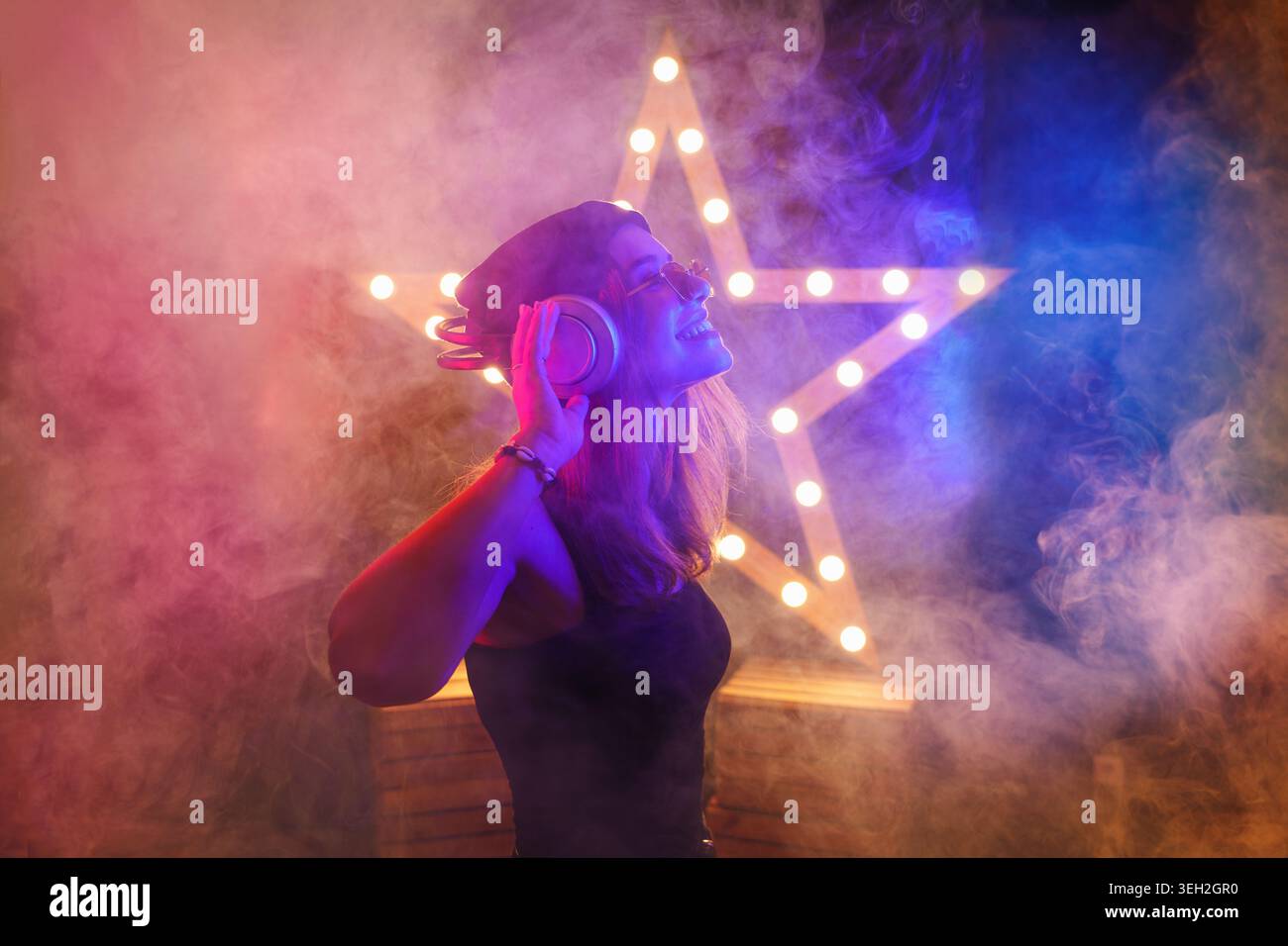 Hintergrundraum mit tanzendem Mädchen in Kopfhörern - Scheinwerfer und Lichter, abstrakter lila Hintergrund mit Neonlicht Stockfoto