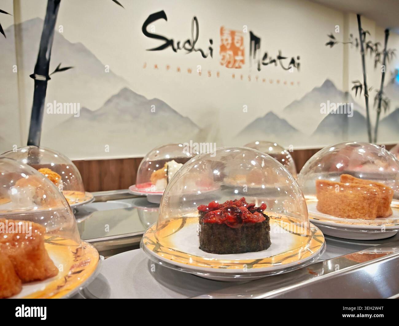 Sushi-Platten, die sich entlang eines Förderbands des Restaurants bewegen, mit verschiedenen Arten von Sushi in klaren Kuppeln Stockfoto