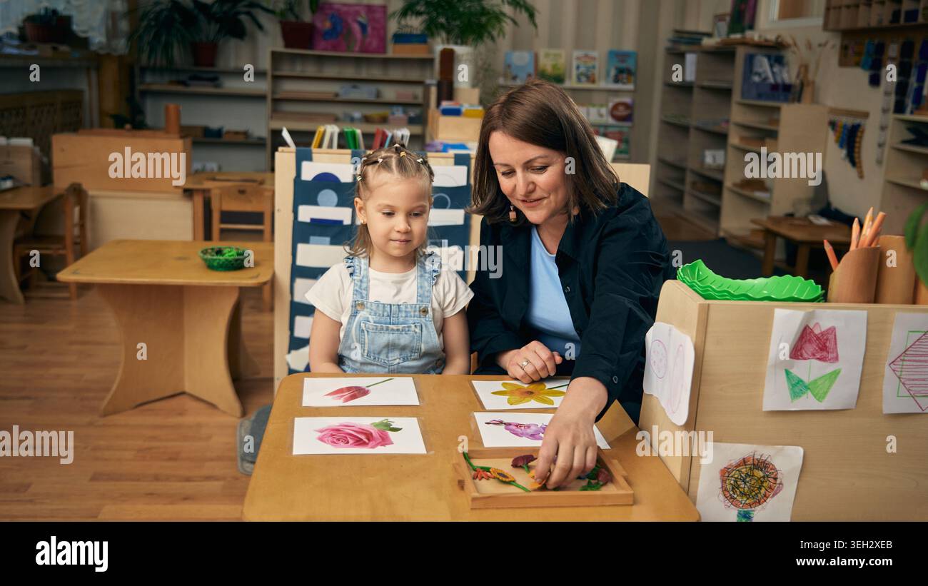 Blumenspiel im Kindergarten mit ruhigem Mädchen und unterstützender Pädagogin. Stockfoto