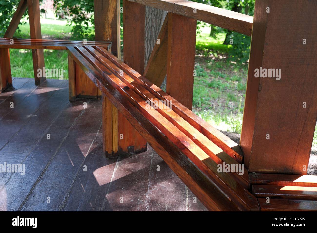 Eine warme Holzbank ruht ruhig unter Bäumen und lädt zu Momenten der Ruhe und des Friedens ein. Stockfoto