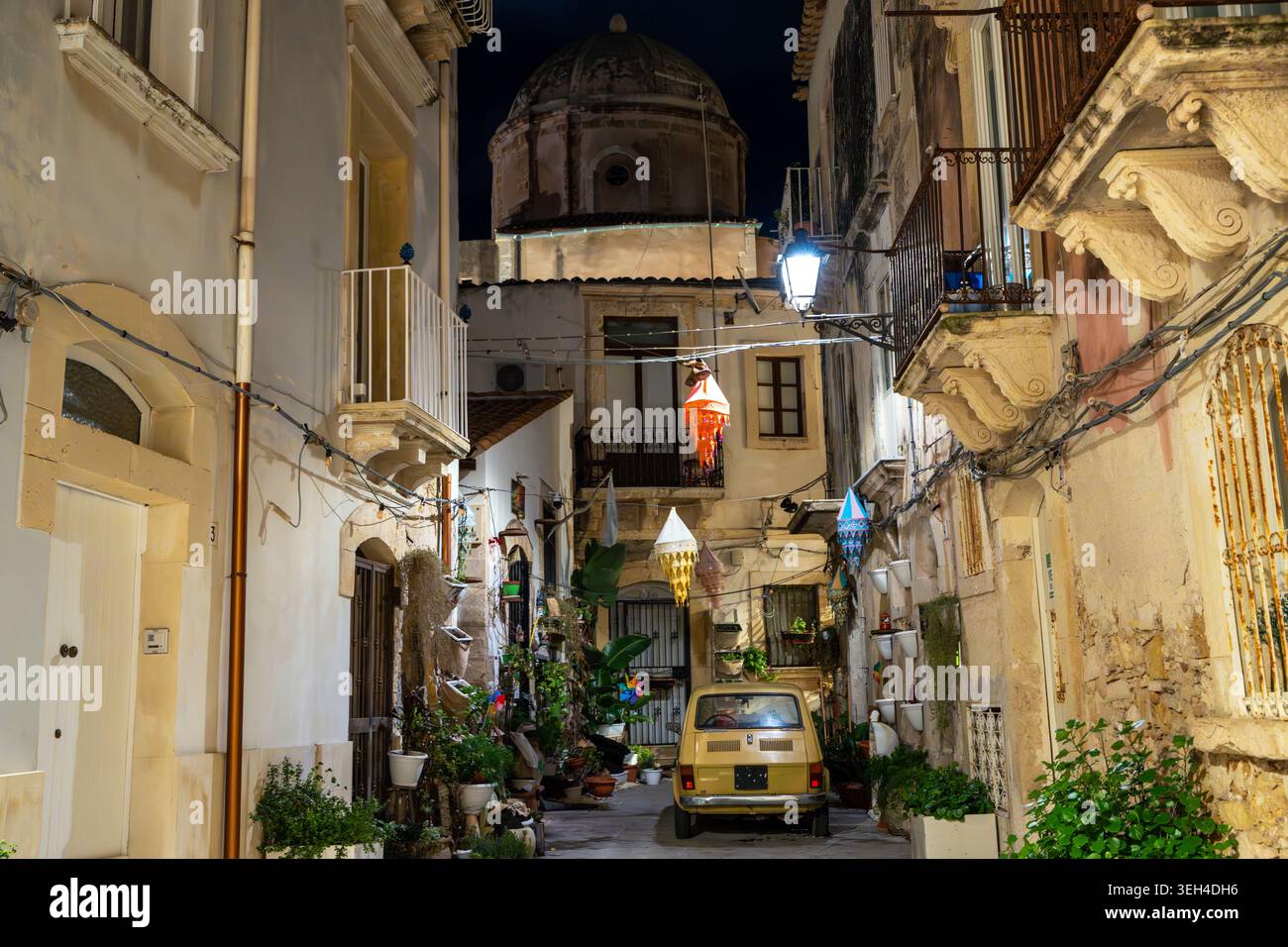 Ein vertikales nächtliches Foto einer bezaubernden engen Straße im historischen Viertel Ortygia, Syrakus. Ein alter gelber Fiat 126 steht im Stockfoto