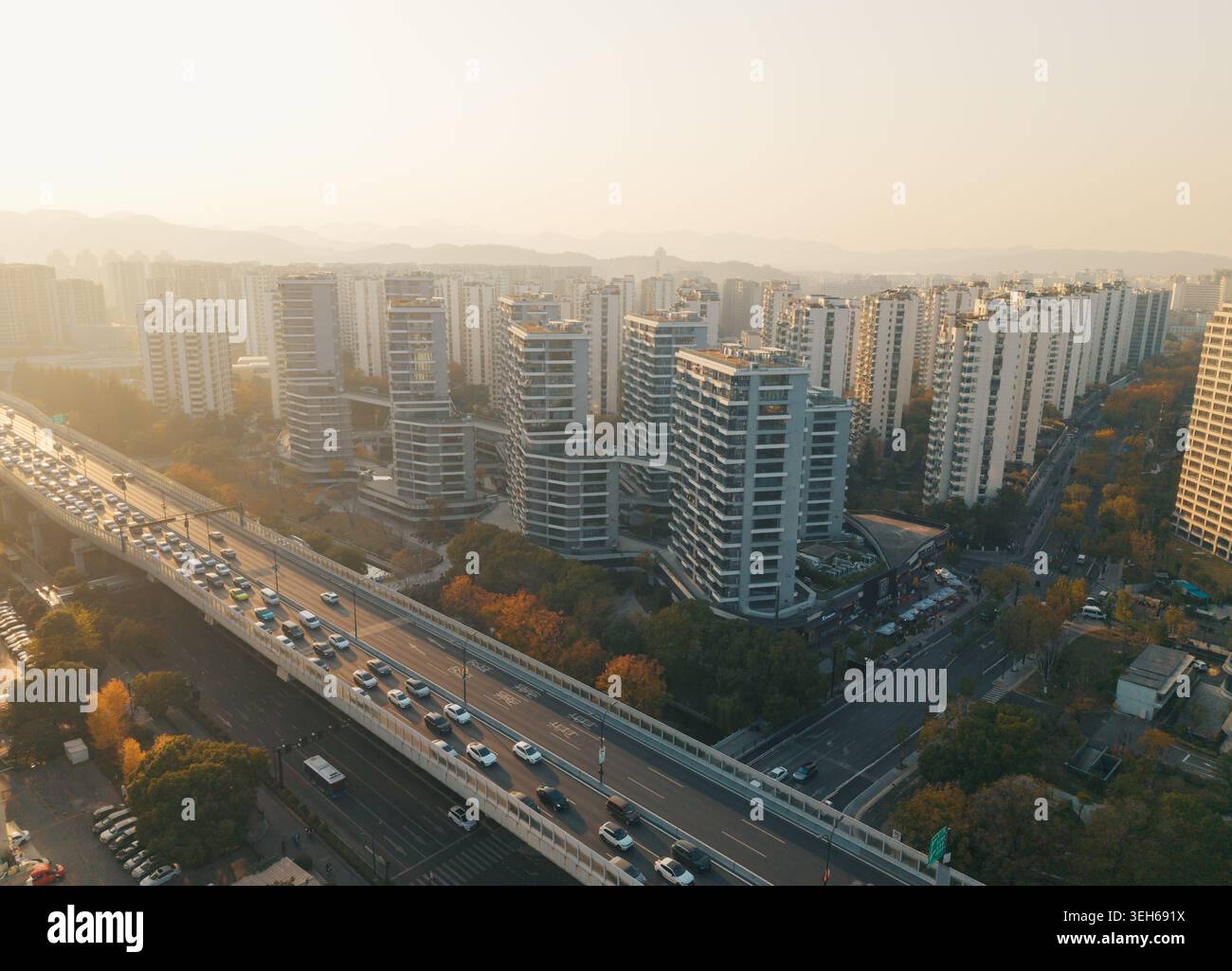 Blick auf die geschäftige Stadt mit einer erhöhten Autobahn, die durch Verkehrsstaus gekennzeichnet ist, umgeben von hoch aufragenden modernen Gebäuden und Bäumen in warmem Licht Stockfoto