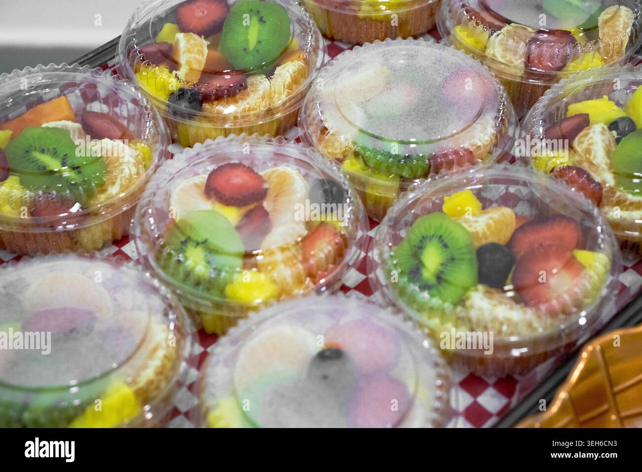 Farbenfrohe Obstkuchen, verpackt in durchsichtigen Kunststoffbehältern, auf einer karierten Oberfläche. Frische Backwaren-Desserts mit Kiwi, Erdbeere und c Stockfoto