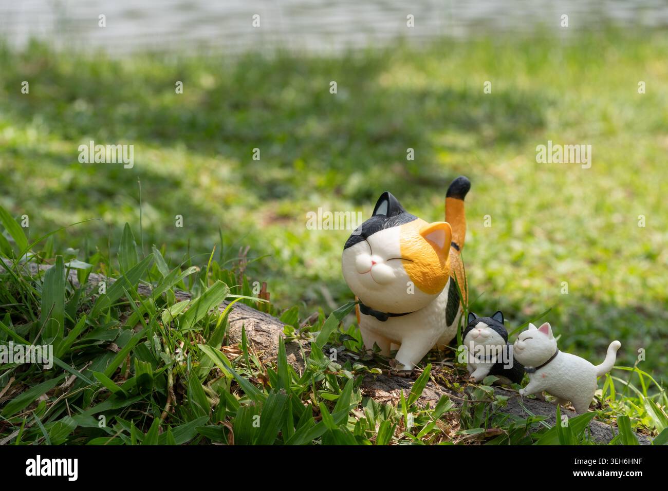 CHIANG Mai, THAILAND - 21. MAI 2026: Große Calico mollige Katzenfigur mit zwei kleinen Katzenfiguren auf Baumwurzel am Reservoir, süßes Kawaii Katzenspielzeug Coll Stockfoto