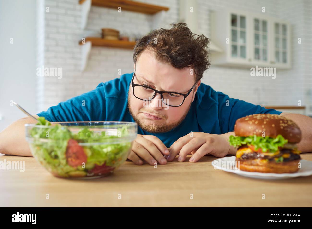 Übergewichtiger Mann, der zwischen gesundem Salat und verlockendem Burger in der Küche zu Hause wählt Stockfoto