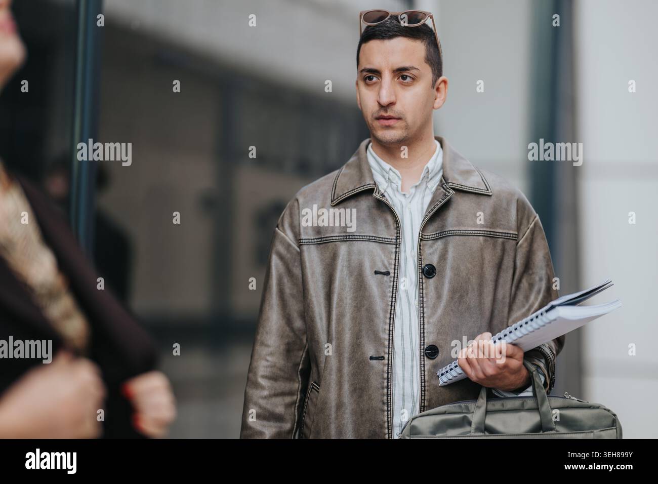 Junger Mann mit Notizbuch und Tasche vor einem Modegeschäft in einer lässigen Lederjacke Stockfoto