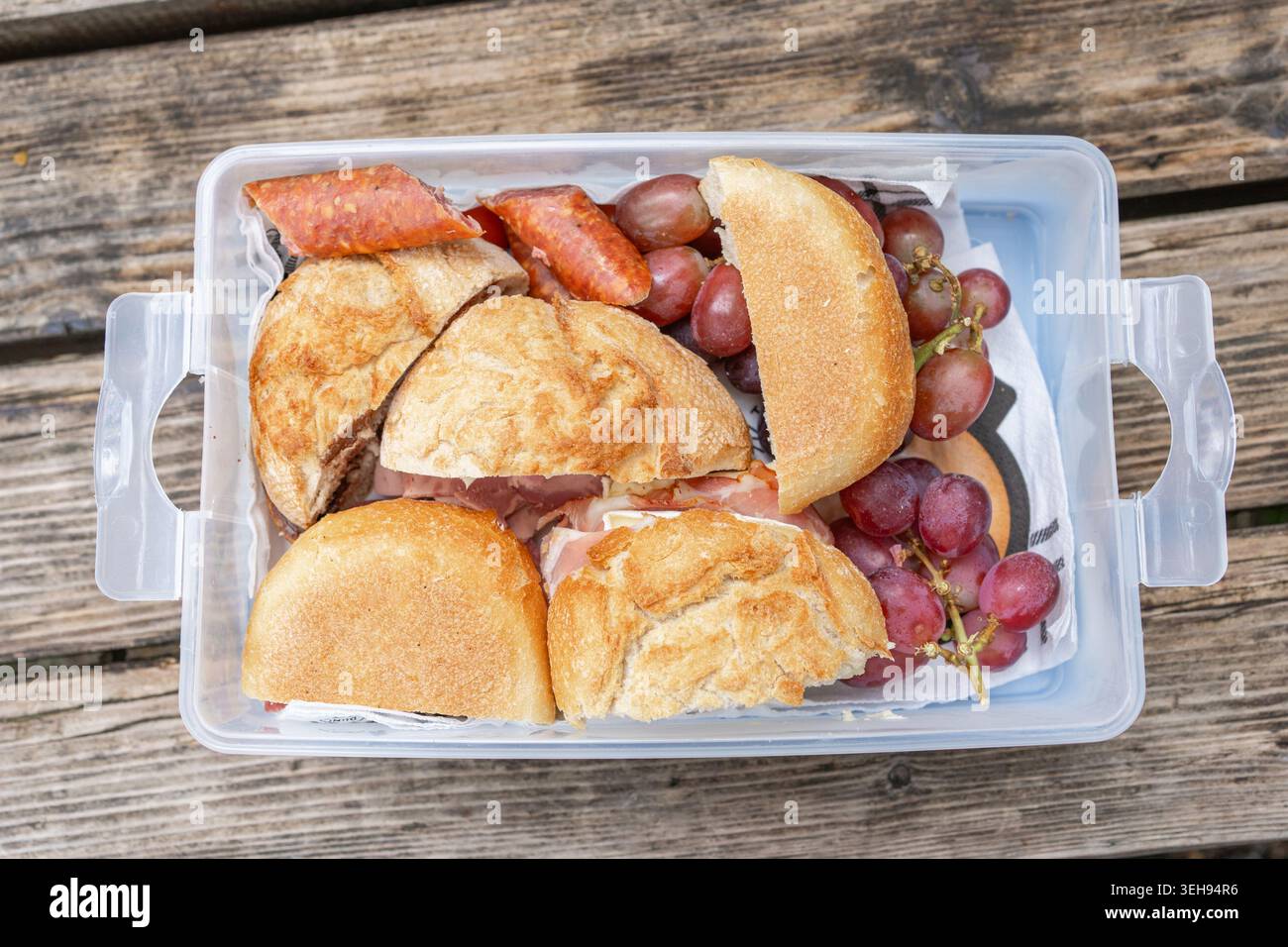 Wander-Snackbox auf einer Holzbank: Lunchbox mit herzhaften Streetfood-Vorspeisen während eines Naturausflugs. Appetitliche herzhafte Mahlzeit, schnelles Mittagessen. Stockfoto