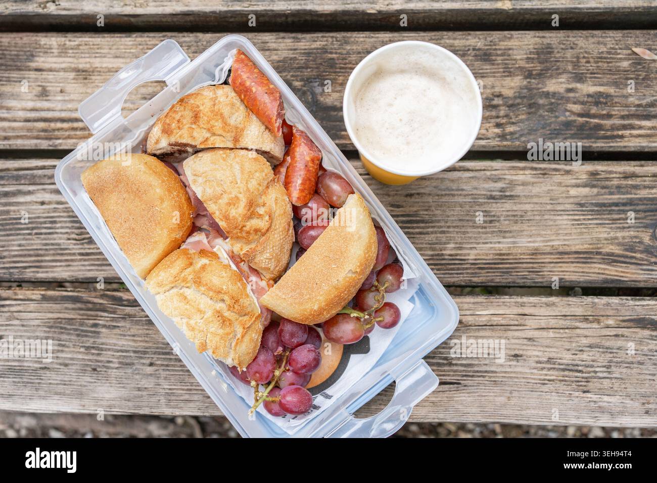 Snack-Set für ein Picknick während einer Reise im Freien. Sandwiches, Würstchen und leichtes Bier auf einer rauen Holztischoberfläche, Freizeit- und Campingkonzept. Stockfoto