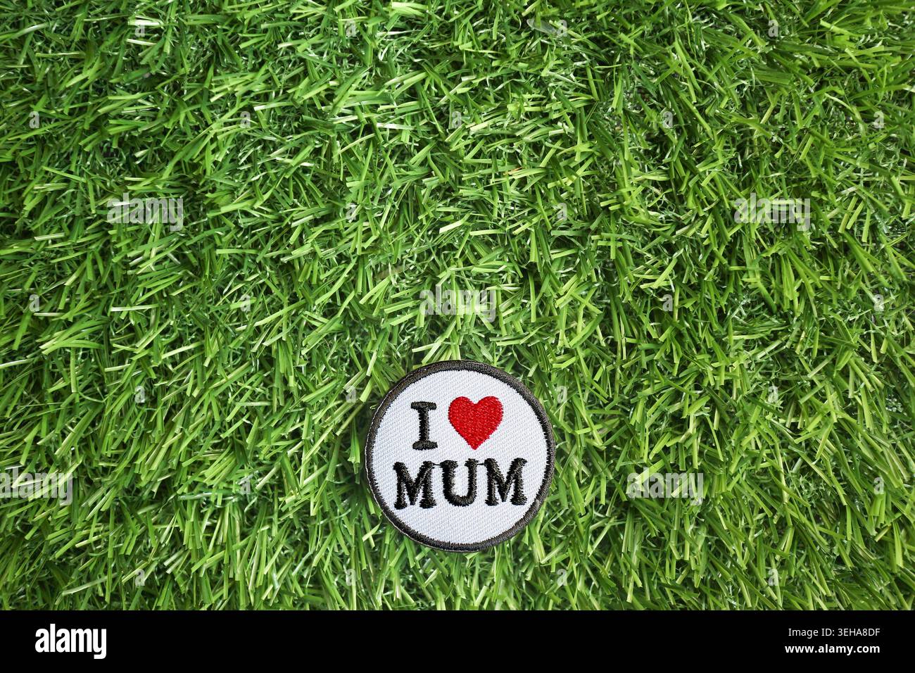 Gestickter I Love Mum Patch auf grünem Grashintergrund, der die Wertschätzung der Mutter und die Zuneigung der Familie symbolisiert. Stockfoto