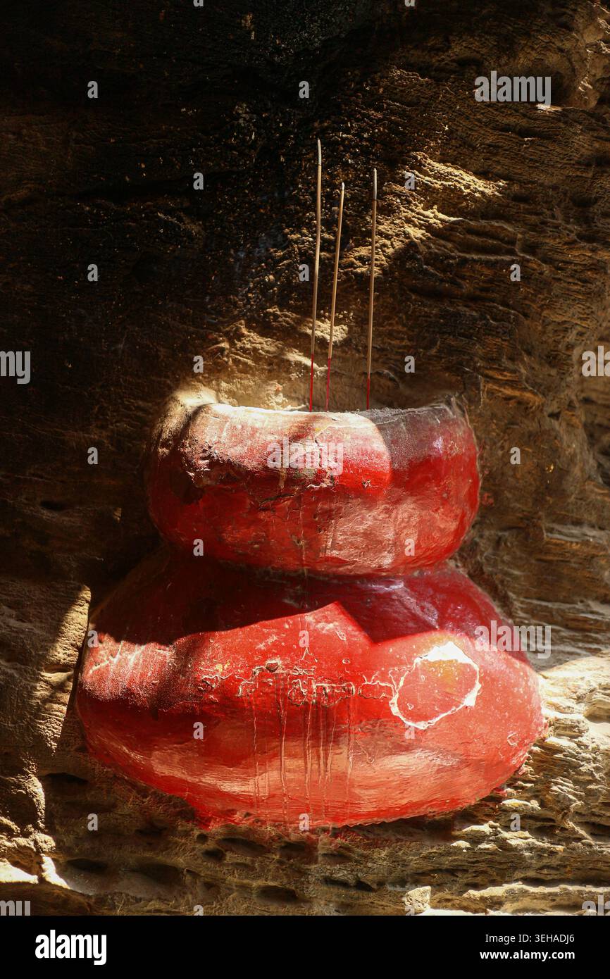 Rote Räucherurne eingebettet in eine Steinklippe an einer heiligen Stätte, die Spiritualität, Tradition und kulturelles Erbe widerspiegelt. Stockfoto