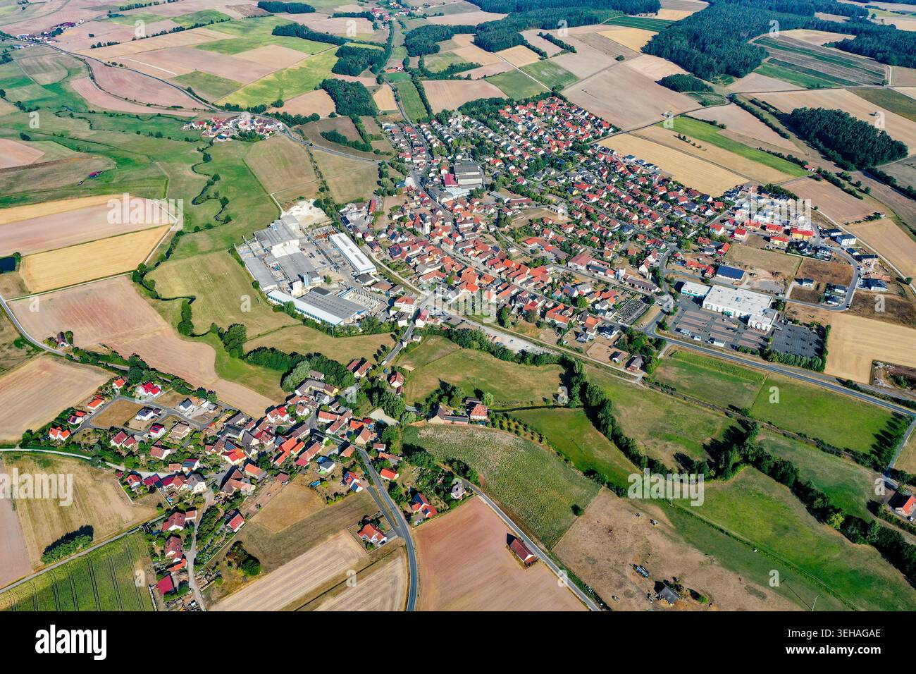 Blick aus der Vogelperspektive auf die Stadt Wachenroth mit roten Häusern, eingebettet zwischen ausgedehnten landwirtschaftlichen Feldern und grünen Wiesen unter klarem Himmel in Wachen Stockfoto