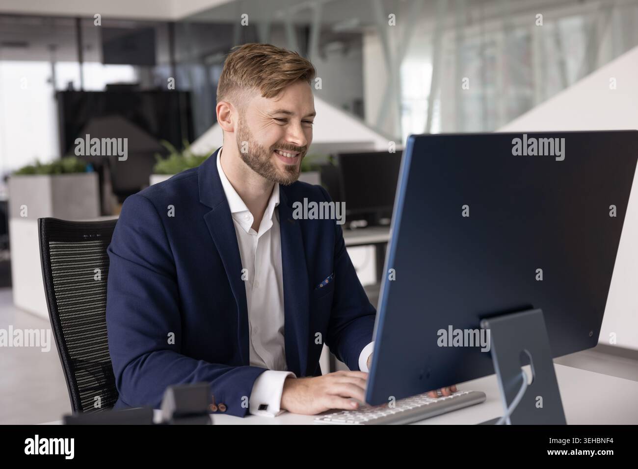 Selbstbewusster junger kaukasischer Geschäftsmann im Anzug, der am Desktop-Computer arbeitet Stockfoto