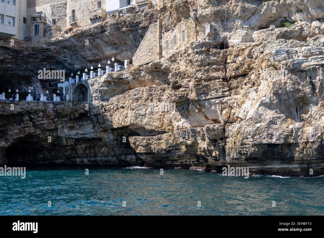 Polignano a Mare, Italien, Apulien - 24. Mai 2024: Gebäude auf Klippen gebaut, Blick vom Meer auf die Felsen und Höhlen von picturesque.Terrasse mit weltberühmter Ruhe Stockfoto