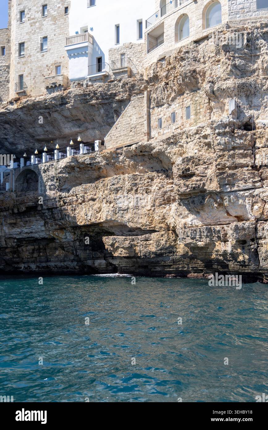 Polignano a Mare, Italien, Apulien - 24. Mai 2024: Gebäude auf Klippen gebaut, Blick vom Meer auf die Felsen und Höhlen von picturesque.Terrasse mit weltberühmter Ruhe Stockfoto