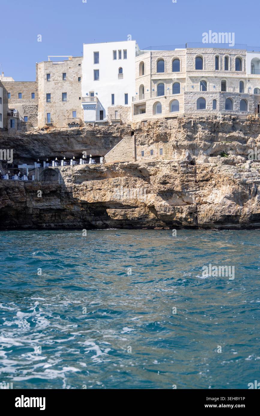 Polignano a Mare, Italien, Apulien - 24. Mai 2024: Gebäude auf Klippen gebaut, Blick vom Meer auf die Felsen und Höhlen von picturesque.Terrasse mit weltberühmter Ruhe Stockfoto