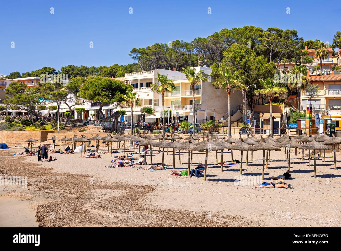 Menschen, die sich an einem Sandstrand mit Sonnenschirm bei einem Küstendorf sonnen Stockfoto