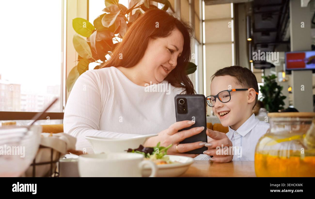 Mutter Teilt Ein Lächeln. Gemeinsamer Moment Beim Frühstück. Mutter Und Sohn Genießen Das Gemeinsame Surfen In Sozialen Netzwerken. Mutter Und Ihr Sohn Erkunden Gerne Die Sozialen Medien Stockfoto