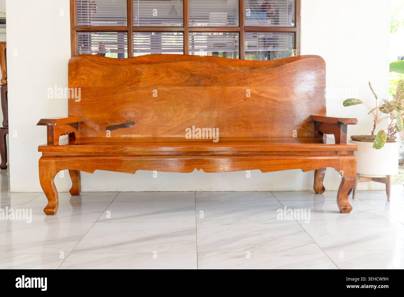 Lange braune Holzbank mit Armlehne wird den Gästen in der Lobby des Hotels oder Resorts serviert. Stockfoto