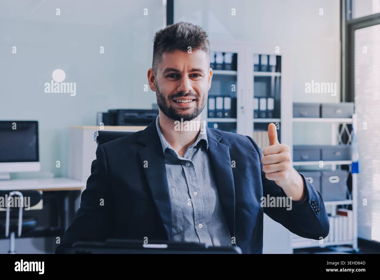 Der lächelnde Geschäftsmann im Anzug arbeitet in einem hellen, modernen Büro mit seinem Laptop Stockfoto