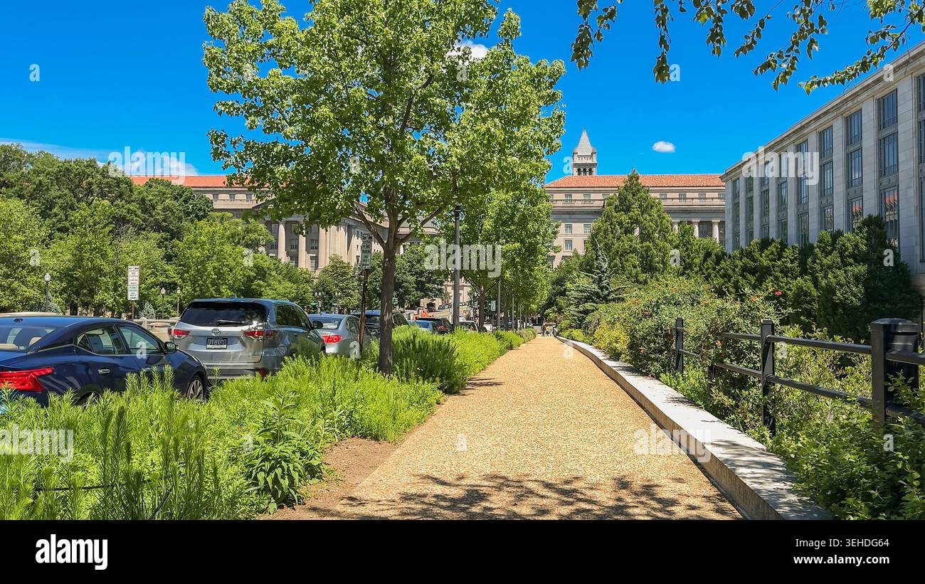 Washington D.C., USA, 25. Mai 2025. Ein ruhiger Pfad verläuft parallel zu einer von Autos gesäumten Stadtstraße, flankiert von historischen Regierungsgebäuden und Bäumen Stockfoto