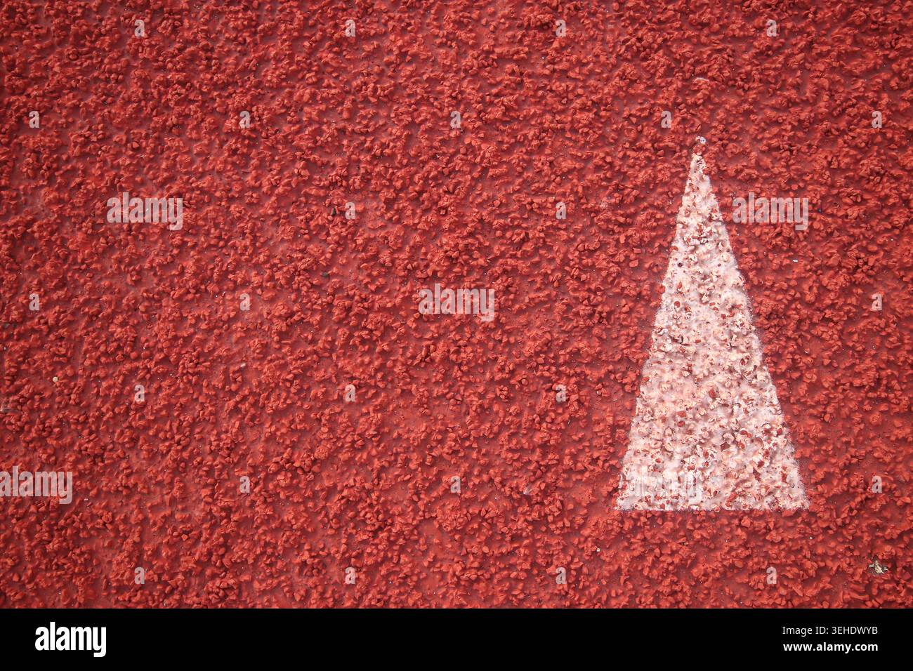 Draufsicht eines weißen, schablonierten Pfeilschildes auf einer roten Streckenoberfläche. Granulierte Textur eines synthetischen Leichtathletikhintergrunds. Stockfoto