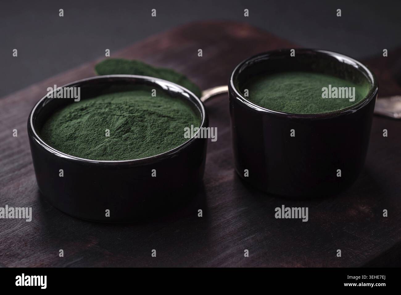 Lebensmittel, Gewürze, grüne Spirulina in Form von Pulver in einer schwarzen Schüssel auf dunklem Betonhintergrund Stockfoto