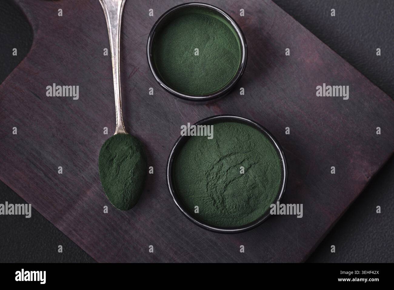 Lebensmittel, Gewürze, grüne Spirulina in Form von Pulver in einer schwarzen Schüssel auf dunklem Betonhintergrund Stockfoto
